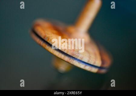 Una foto macro di un teetotum in legno che gira e si trova su una superficie di vetro, che mostra la sua intricata maestria artigianale e la superficie liscia e riflettente. Foto Stock