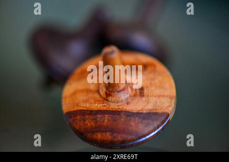 Una foto macro di un teetotum in legno che gira e si trova su una superficie di vetro, che mostra la sua intricata maestria artigianale e la superficie liscia e riflettente. Foto Stock