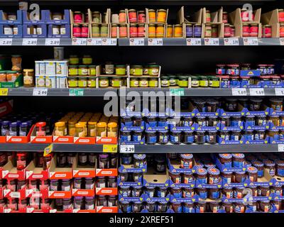 Uno scaffale con molti vasetti di marmellata diversi. Gli scaffali del supermercato sono rivestiti con vasetti di diversi tipi di marmellata. Le marmellate hanno una forma diversa Foto Stock