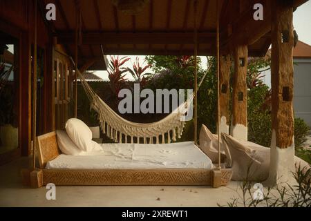 Tabanan, Bali, Indonesia - 9 agosto 2024: Terrazza patio di una moderna villa in legno in stile rustico con mobili da esterno, un letto altalena e un mac Foto Stock