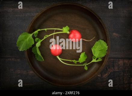 Due ravanelli rossi con foglie su un piatto di legno Foto Stock