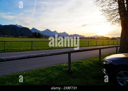 Strada romantica che conduce attraverso i verdi e panoramici prati alpini delle Alpi Bavaresi in una serata di primavera soleggiata e tranquilla (Allgaeu, Schwangau) Foto Stock