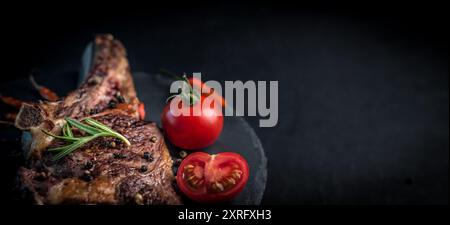 Primo piano di bistecca di manzo grigliata su osso con pomodori sul tagliere in pietra con spazio per copiare Foto Stock