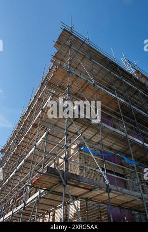 Ponteggi con piattaforme contro un alto complesso di appartamenti di nuova costruzione in un cantiere. Cielo blu Foto Stock