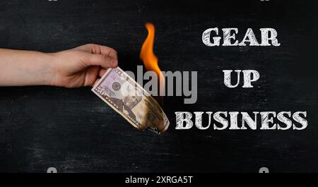 Una mano che regge un banconota da un dollaro con le parole Gear Up Business scritte sotto di essa. Concetto di avvio di un'attività e l'importanza di essere preparati e. Foto Stock