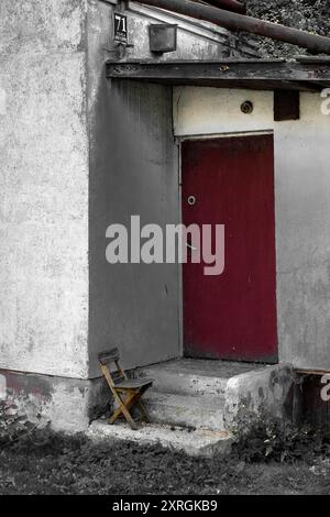 Sedia di legno di un bambino dimenticato fuori da una casa abbandonata a Opoczno, Polonia. Povertà, decadimento, povertà. Immagine parzialmente desaturata. Foto Stock