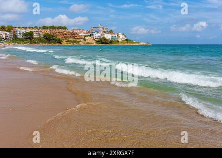 Onde dolci che scivolano sulla spiaggia sabbiosa con residenze costiere a Tarragona, Spagna Foto Stock