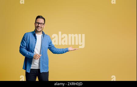 Ritratto di un venditore felice che mostra qualcosa sul palmo mentre si sta in piedi su sfondo giallo Foto Stock
