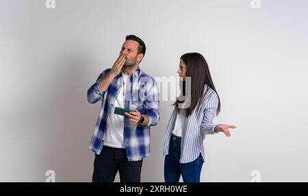 Donna arrabbiata che gesta e guarda l'uomo estatico del giocatore che soffia bacio mentre gioca ai videogame su un telefono cellulare. Fidanzata seria che fissa il ragazzo felice Foto Stock