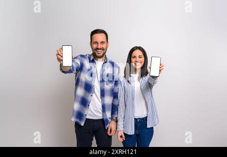 Giovane coppia sorridente e mostra schermi vuoti di smartphone per la pubblicità. Uomo e donna allegri che promuovono telefoni cellulari con spazio libero vuoto A. Foto Stock