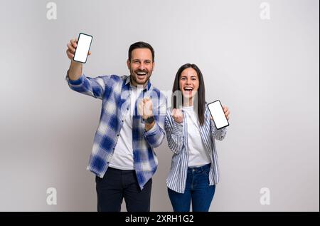 Allegra fidanzata e fidanzato che pompano pugni di gioia e mostrano smartphone per il marketing. Giovane coppia vestita di casuali urlando e festeggiati Foto Stock