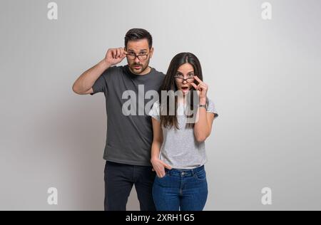 Una giovane coppia stupita con occhi e bocca spalancati che guardano gli occhiali alla telecamera. Uomo e donna scioccati vestiti di casuali ascoltando inaspettati Foto Stock