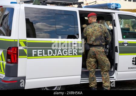 Augusta, Baviera, Germania - 10 agosto 2024: Un ufficiale di polizia militare delle forze armate tedesche in uniforme mimetica si trova di fronte a un veicolo di polizia militare. Immagine simbolica dell'ordine militare e della sicurezza fornita dalla polizia militare della Bundeswehr *** Ein Feldjäger der Bundeswehr a Tarnuniform steht vor einem Feldjägerfahrzeug. Symbolbild militärische Ordnung und Sicherheit, die durch die Militärpolizei der Bundeswehr gewährleistet wird Foto Stock