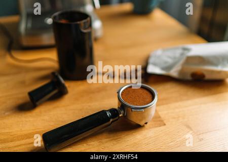 Un portafiltro riempito con caffè appena macinato su un piano di legno con un macinacaffè e chicchi sullo sfondo. Foto Stock