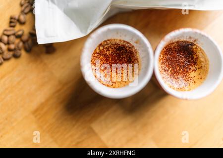 Vista dall'alto di due tazze di espresso appena preparato con chicchi di caffè su un tavolo di legno. Foto Stock
