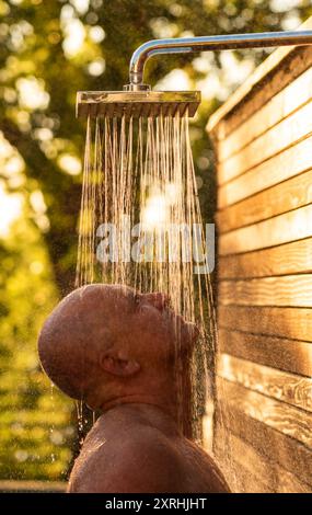 Uomo che fa una doccia rinfrescante all'aperto al tramonto. Concetto di relax e benessere Foto Stock