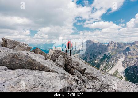 Donna escursionista in piedi in Hero posa su una roccia sulla vetta della montagna guardando il paesaggio alpino in una giornata nuvolosa Foto Stock
