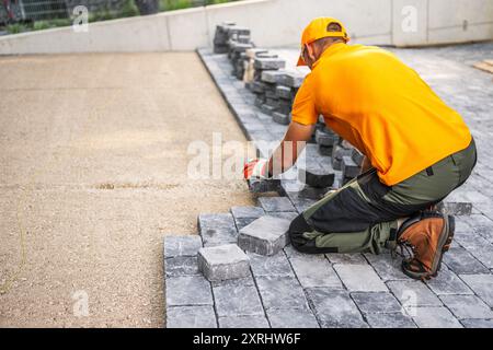 Un operaio edile posiziona con cura i ciottoli per creare un nuovo patio in un cortile residenziale sotto la luce del sole. Foto Stock