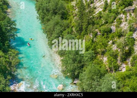 Due kayak navigano in un vivace fiume turchese del fiume Soca, fiancheggiato da fitte foreste e scogliere rocciose in una giornata di sole. Foto Stock