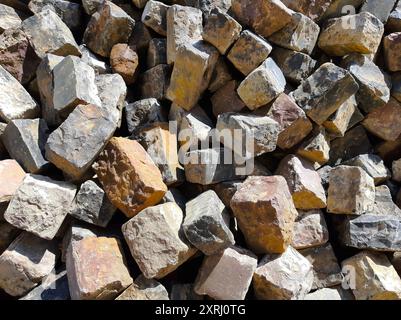Vari mattoni con texture uniche impilati insieme in un'area illuminata dal sole, pronti per l'uso. Foto Stock