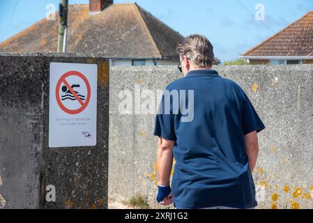 Un camminatore è visto passare accanto a un Consiglio contro il cartello del bagno a St Mary's Bay. Consigli e cartelli contro il nuoto sono stati posti intorno alla spiaggia di St Mary's Bay nel febbraio 2023 a causa degli alti livelli di inquinamento che sono stati indicati da campioni di qualità dell'acqua fatti dalle agenzie ambientali. Foto Stock