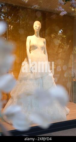 Manichino in elegante abito da sposa bianco, vetrina da sogno con riflessi floreali, romantica vetrina di moda in soffice luce dorata Foto Stock