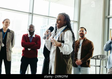 Donna sicura di sé che parla a una conferenza con i colleghi in un ufficio moderno. Presentazione di idee a colleghi impegnati e diversi. Foto Stock