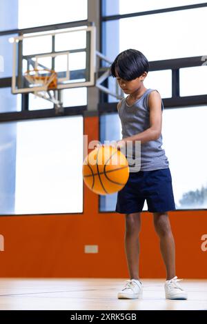 Dribbling basket, ragazzo che pratica nella palestra scolastica, concentrandosi sulle abilità Foto Stock