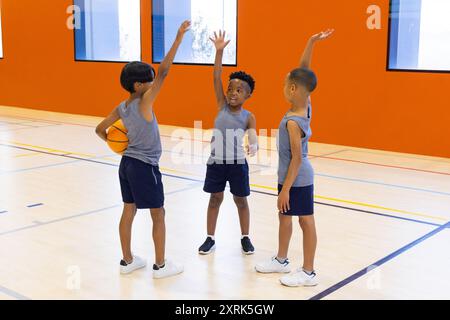 Giocando a basket, tre ragazzi in palestra a scuola che si allenano a vicenda Foto Stock
