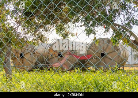 Grandi serbatoi di stoccaggio industriali si trovano dietro una recinzione a maglie di catena sormontata da filo spinato Foto Stock