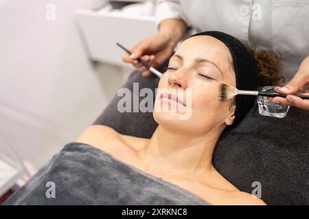 Estetista del raccolto che applica olio detergente al cliente nel centro di bellezza Foto Stock