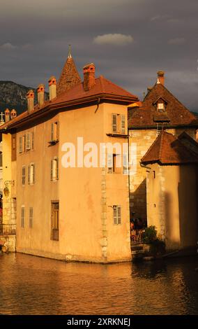 Case sul canale nella pittoresca città vecchia di Annecy (Francia) al tramonto dorato in giornata nuvolosa. Maestoso gioco di luci e ombre contrastanti. Foto Stock