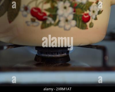 Primo piano orizzontale di un bruciatore a gas acceso sotto una pentola di cottura gialla con stampa Cherry Foto Stock