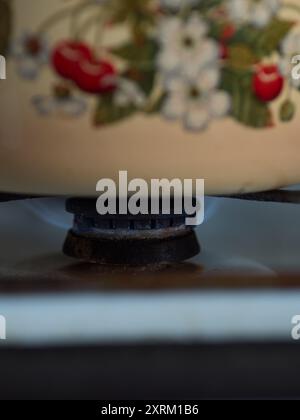 Primo piano verticale di un bruciatore a gas acceso sotto una pentola di cottura gialla con stampa Cherry Foto Stock