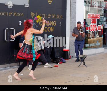 L'uomo suona un violino come una donna in gonne tartan a Price Street durante il Fringe Festival di Edimburgo in Scozia. 10 agosto 2024 Foto Stock