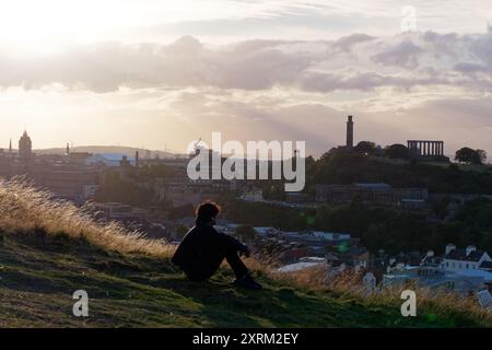 Man gode di una vista da Salisbury Crags verso Calton Hill con il National Monument e il Nelsons Monument. Edimburgo, capitale della Scozia, 10 agosto 2024 Foto Stock