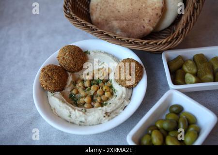 Hummus, piatto mediorientale a base di purea di ceci cotti mescolati con tahini, succo di limone e aglio, pita, palline di falafel, cetrioli sottaceto e olive Foto Stock