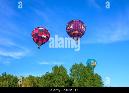 Palloncini colorati illuminati dal sole nell'ora d'oro, dalla festa in mongolfiera di Bristol del 2024 mentre passano sopra gli alberi vicino a Siston; Bristol. Scattate alle 19.45, sabato Foto Stock