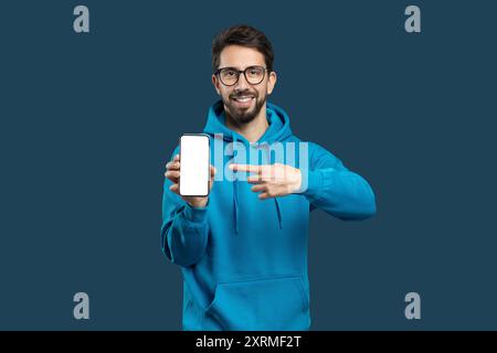 Young Man in Hoodie mostra smartphone mentre sorride alla fotocamera Foto Stock