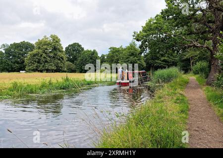 Una barca stretta che naviga sul canale di navigazione del fiume Wey vicino a Byfleet, in una giornata estiva Surrey Inghilterra Regno Unito Foto Stock