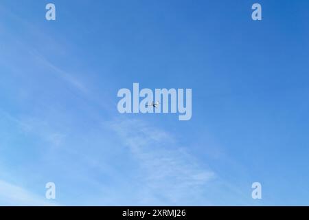 L'aereo vola in alto nel cielo blu con piccole nuvole Foto Stock