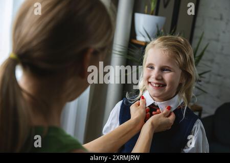 la madre aiuta e aiuta sua figlia a prepararsi per il primo giorno di scuola nel salotto di casa Foto Stock