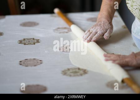 primo piano dell'impasto rugoso delle vecchie mani della nonna con un mattarello. Donna anziana che stira l'impasto con un mattarello Foto Stock