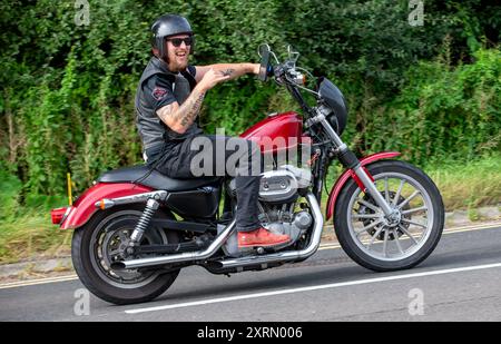 Potterspury, Northants, Regno Unito - 11 agosto 2024: Uomo a bordo di una moto Harley Davidson XL883 rossa che viaggia su una strada britannica Foto Stock