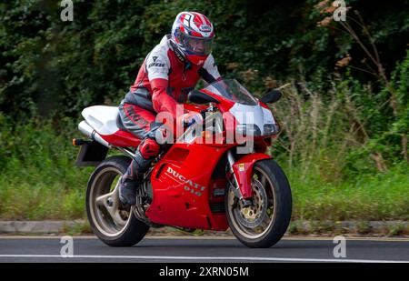 Potterspury,Northants,UK - 11 agosto 2024: Uomo a bordo di una moto Ducati 916 rossa che viaggia su una strada britannica Foto Stock