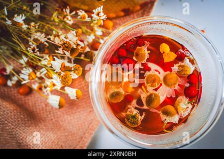 Una tazza di tè alle erbe con spinoso marino e mirtilli sul tavolo con un tovagliolo di tela e fiori di camomilla. Foto di alta qualità Foto Stock