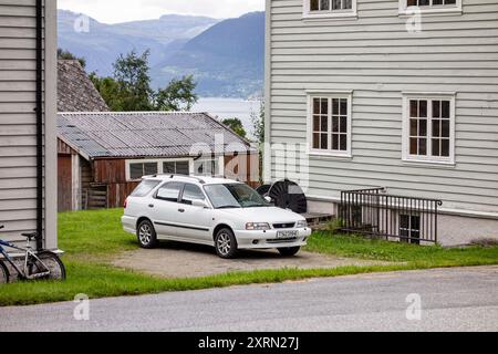 KINSARVIK, NORVEGIA - 10 AGOSTO 2016: Suzuki Baleno Wagon bianca parcheggiata in Norvegia accanto a case di legno Foto Stock