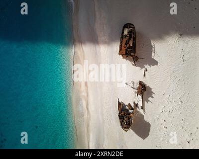 Vista aerea di un naufragio su una spiaggia sabbiosa con acque blu cristalline, che mostra il contrasto tra la nave arrugginita e i dintorni incontaminati. Foto Stock