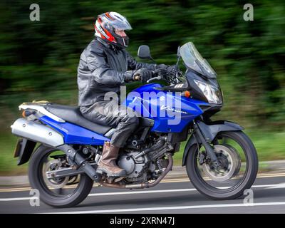 Potterspury, Northants, Regno Unito - 11 agosto 2024: Uomo a bordo di una Suzuki V-Strom blu che viaggia su una strada britannica Foto Stock