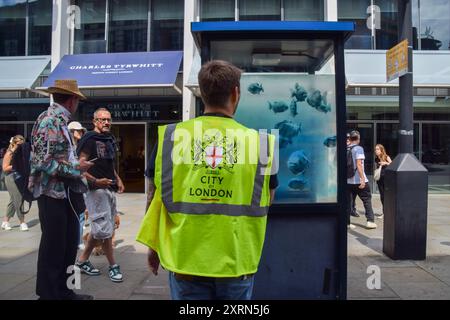 Un operaio ispeziona la scatola di sentinelle della polizia nella City di Londra con la nuova opera d'arte di Banksy che raffigura una scuola di pesci. Questa è la settima nuova opera d'arte a tema animale in sette giorni nella capitale dall'elusivo artista di strada. Foto Stock